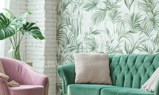 Ein grünes Samtsofa und ein rosafarbener Sessel mit einer Monstera-Pflanze. Die Wand hinter dem Sofa ist mit einer tropischen Tapete mit Palmenblättern dekoriert, eine tolle Idee, um zwei Tapeten zu kombinieren.