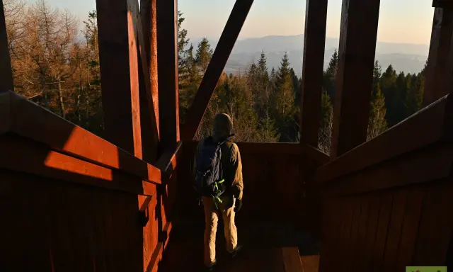 Turysta wchodzi po drewnianych schodach na wieżę widokową, podziwiając panoramę gór.