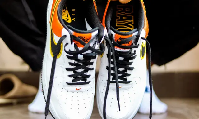 Białe buty Nike Air Force 1 z pomarańczowo-żółtymi akcentami. Sprawdź metkę i logo, by dowiedzieć się, jak sprawdzić czy buty są oryginalne.
