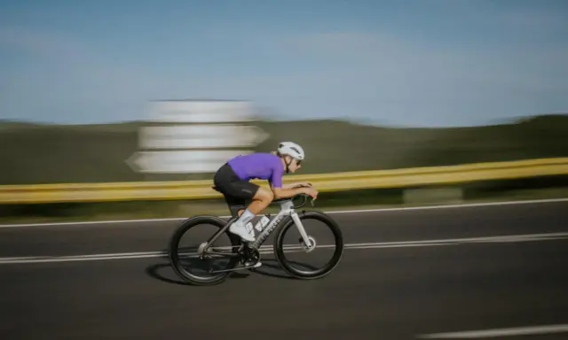 Kolarz w fioletowej koszulce pędzi na rowerze, osiągając prędkość 50 km/h.