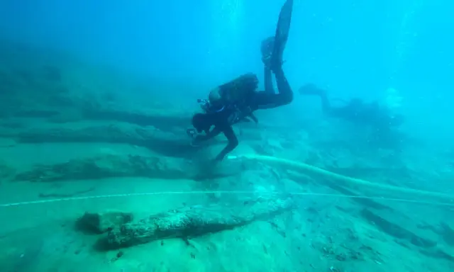 Subacquei esplorano un sito archeologico subacqueo, tra antichi resti di legno. Un'immersione per scoprire cosa vedere.