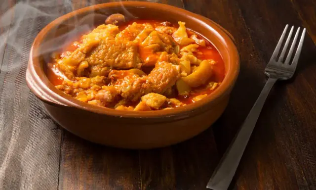 Un plat fumant de tête de veau mijotée dans une sauce rouge, rappelant la recette tête de veau grand-mère. Une fourchette est posée à côté.