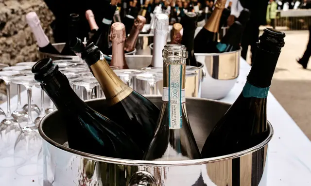 Mehrere Flaschen Sekt in einem silbernen Eiskübel, bereit für die Feier. Gläser stehen daneben.