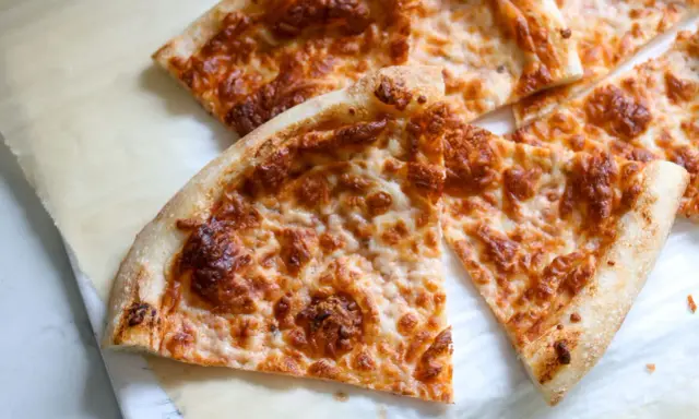 Tranches de pizza au fromage doré, préparées avec un levain rafraichi, sur du papier sulfurisé.