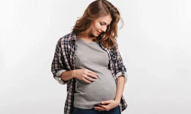 Kobieta w ciąży delikatnie dotyka brzucha. Częste oddawanie moczu w ciąży to normalny objaw.