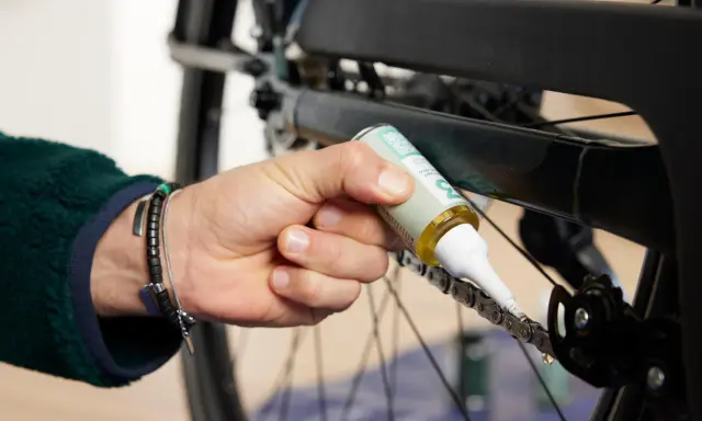 Dłoń z buteleczką oleju aplikuje go na rowerowy łańcuch, dbając o jego płynne działanie. Czyszczenie łańcucha rowerowego to klucz do sprawnej jazdy.