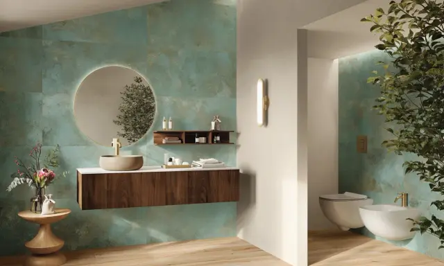 Elegante bagno verde petrolio e legno con lavabo in pietra, specchio rotondo e bidet sospeso.