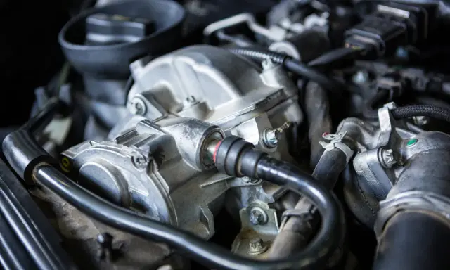 Primer plano del motor de un coche, mostrando el alternador y otras piezas. Podría ser la causa de un fallo alternador coche.
