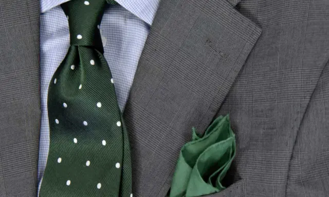 Zielony krawat w kropki do niebieskiej koszuli i szarej marynarki. Elegancka stylizacja.