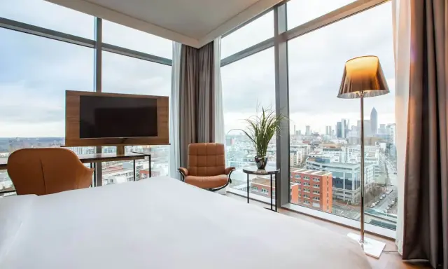 Modern Hotelzimmer mit Skyline-Blick, Bett, Sessel und Fernseher.