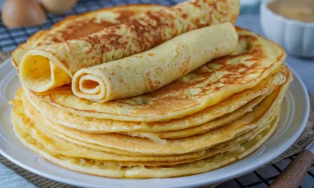 Ein Stapel goldbrauner Eierkuchen, zwei davon gerollt, perfekt für ein einfaches Eierkuchen Rezept.