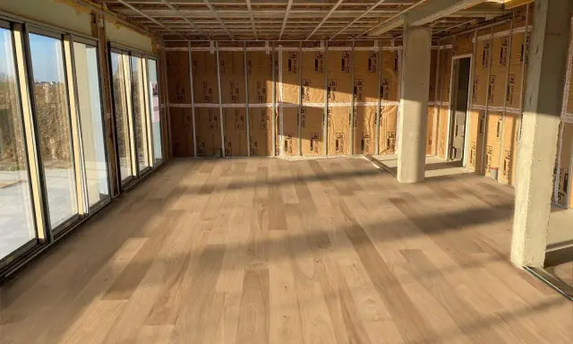 Pose de parquet clair dans une pièce en construction, le sens des lames semble agrandir l'espace.