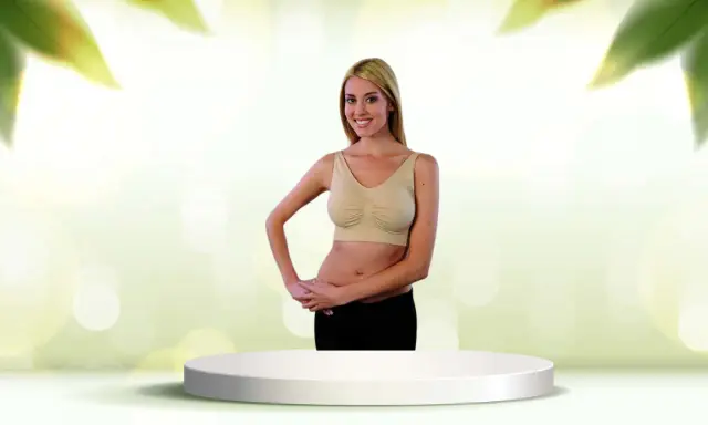 Donna sorridente con tette e reggiseno beige, in piedi su un piedistallo bianco.
