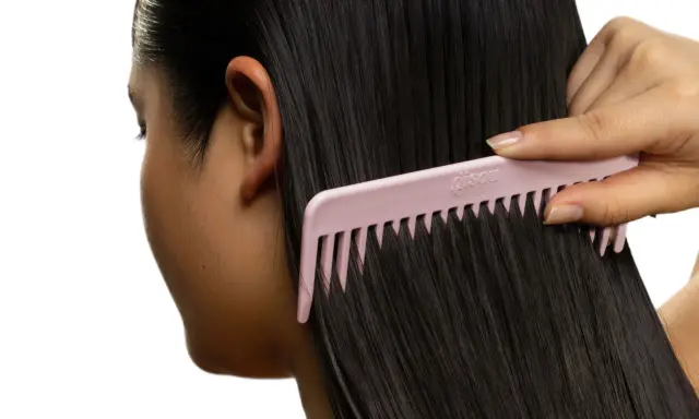 Une main peigne des cheveux noirs et brillants avec un peigne rose. Le peigne est large et espacé, idéal pour démêler les cheveux sans les casser, évitant ainsi les cheveux emmêlés cause.