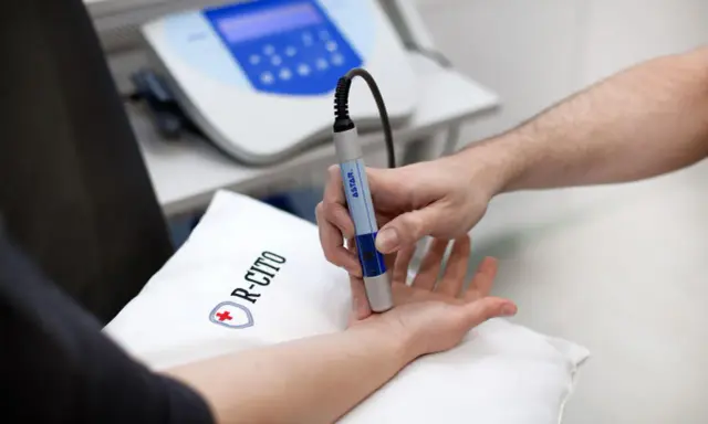 Fizjoterapeuta wykonuje zabieg laserem na dłoni pacjenta.