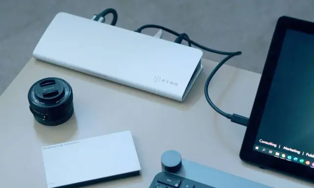 Stacja dokująca ICY BOX podłączona do laptopa, obok obiektyw Sony i dysk Porsche Design.
