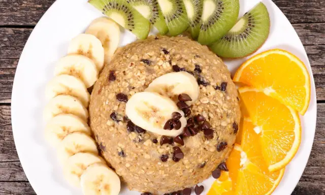 Un délicieux bowl cake flocon d'avoine, garni de rondelles de banane, de tranches de kiwi et d'orange, parsemé de pépites de chocolat.