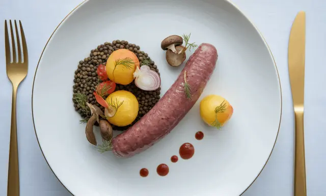 Une saucisse de Toulouse savoureuse, accompagnée de lentilles, de tomates cerises, de champignons et de petites pommes de terre dorées.