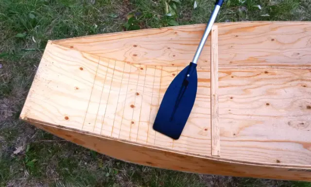 Bateau en contreplaqué brut, prêt pour la résine époxy. Une pagaie noire repose à l'intérieur.