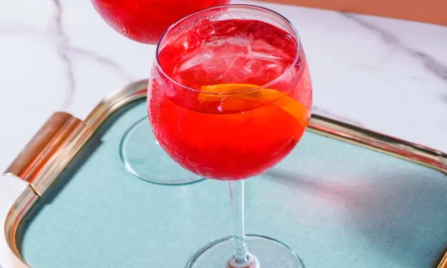 Ein erfrischender Campari Spritz mit Eis und Orangenscheibe auf einem Tablett.