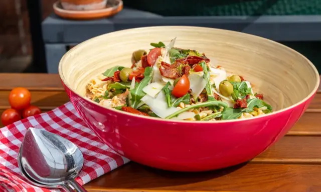 Leckere nudelsalat ideen: Pasta mit Rucola, Tomaten, Oliven und Parmesan in einer roten Schüssel.