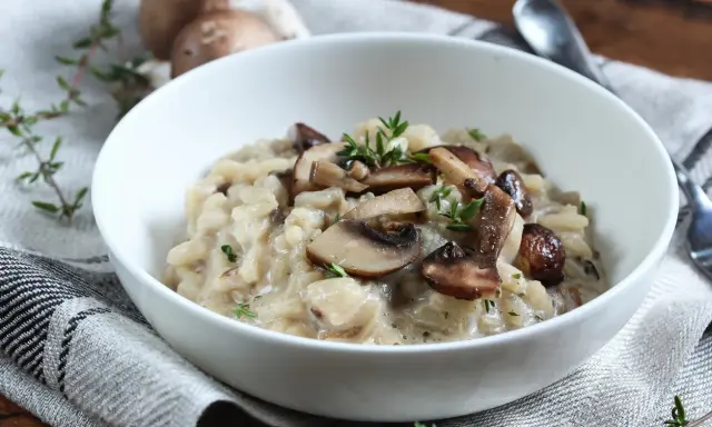 Aksamitne risotto z pieczarkami, udekorowane świeżym tymiankiem, w białej misce na lnianej serwetce.