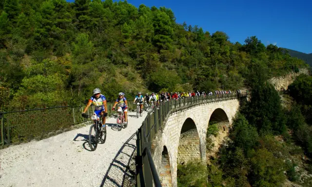 Ciclisti in gruppo percorrono la ciclabile Spoleto Norcia su un viadotto panoramico, immersi nel verde.