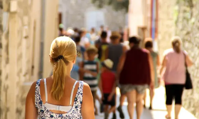 Kobieta z blond kucykiem idzie wąską uliczką pełną ludzi, odkrywając urokliwe villach atrakcje.