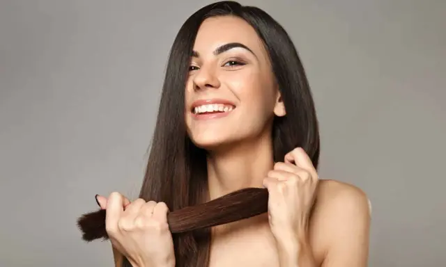 Mujer sonriente muestra su cabello largo y sedoso, un ejemplo de cómo cuidar el pelo para que luzca saludable y brillante.