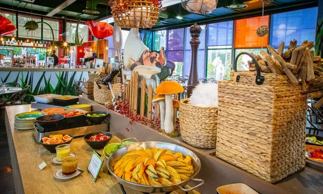 Buffet coloré avec des plats de courges, salades et fruits. Décoration ludique avec des champignons et un personnage de conte de fées, dans l'ambiance du resto Futuroscope.