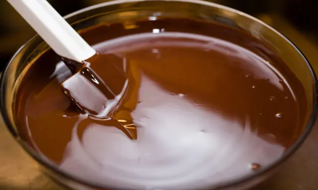 Spatule blanche remuant du chocolat fondu dans un bol en verre. Le chocolat est lisse et brillant, prêt à être utilisé pour une recette.
