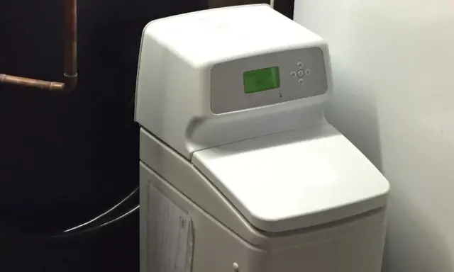 Adoucisseur d'eau blanc avec écran vert, un avantage pour une eau plus douce et une maison protégée.