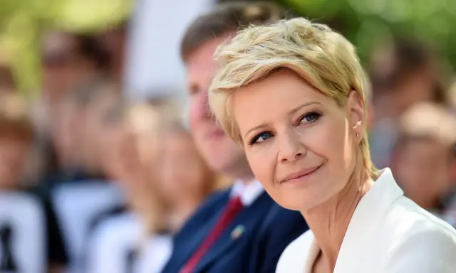 Kobieta z blond włosami w super krótkiej fryzurze damskiej, w białej marynarce, uśmiecha się.