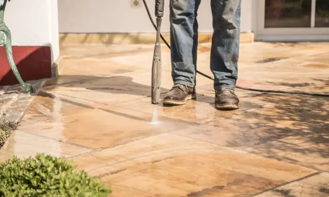Nettoyer carrelage extérieur noirci avec un nettoyeur haute pression. L'eau projetée révèle la beauté naturelle des dalles.