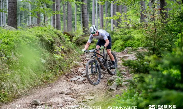 Kolarz MTB pokonuje kamienisty zjazd w lesie. To fragment kalendarza MTB, pełnego adrenaliny i pasji.