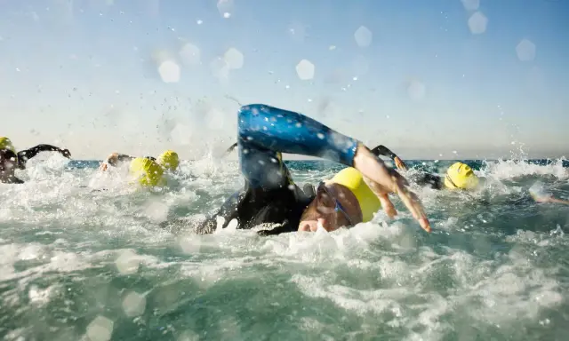 Schwimmer mit gelben Kappen kämpfen sich durch die Wellen. Die triathlon strecken sind anspruchsvoll.