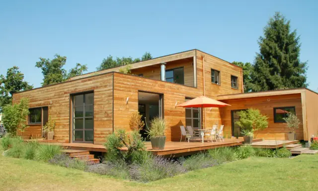 Maison moderne en bois avec terrasse et jardin. La construction maison ossature bois met en valeur le matériau naturel.