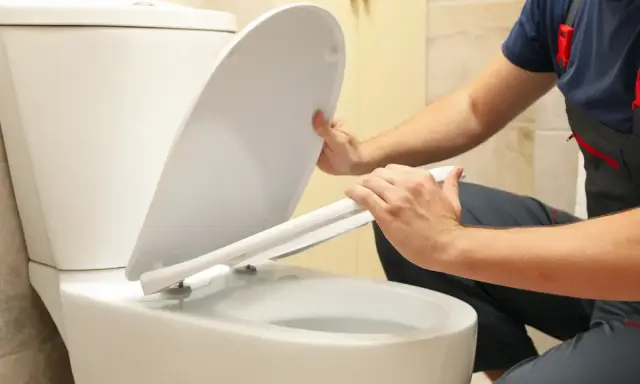 Un plombier en salopette commence à démonter la cuvette de toilette.