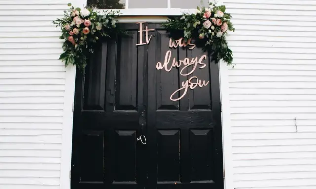 Elegancka dekoracja domu pana młodego: czarne drzwi ozdobione kwiatami i napisem "It was always you".
