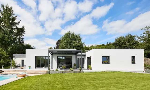Une maison modulable moderne avec piscine et jardin luxuriant, sous un ciel bleu éclatant.