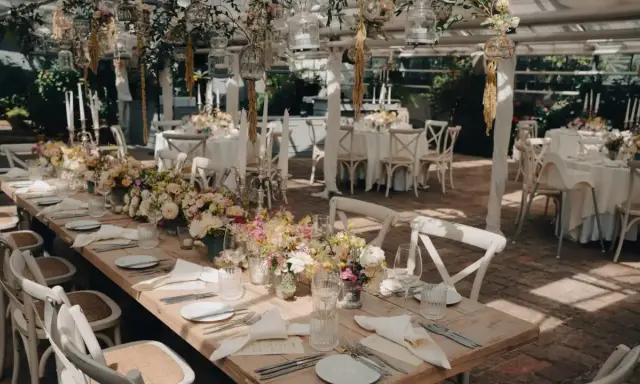 Romantische Hochzeitslocation Ideen: Ein langer Holztisch mit Blumenarrangements, Kerzen und weißen Stühlen, bereit für Gäste.