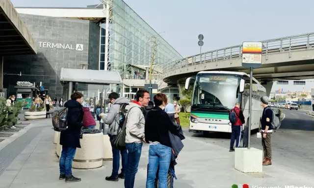 Ludzie czekają na autobus przed Terminalem A na lotnisku w Katanii.