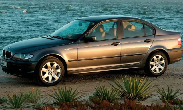 Szary sedan BMW E4 na plaży, z morzem w tle.