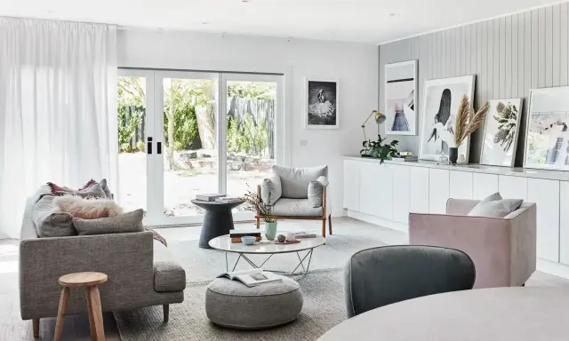 Elegante salón con sofás grises y rosas, mesa de centro y **cuadros apoyados en muebles** de la pared.