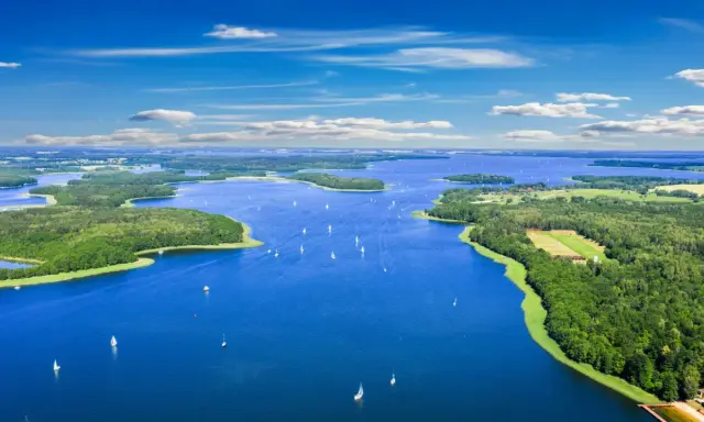 Malownicze mazury jeziora z licznymi wyspami i żaglówkami pod błękitnym niebem.