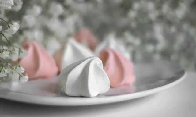 Douceur aérienne de meringue italienne rose et blanche sur une assiette, avec des petites fleurs en arrière-plan.