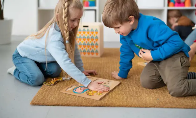 Dzieci na dywanie układają puzzle, ćwicząc spostrzegawczość. To nauka przez zabawę, zgodna z metodą Montessori.