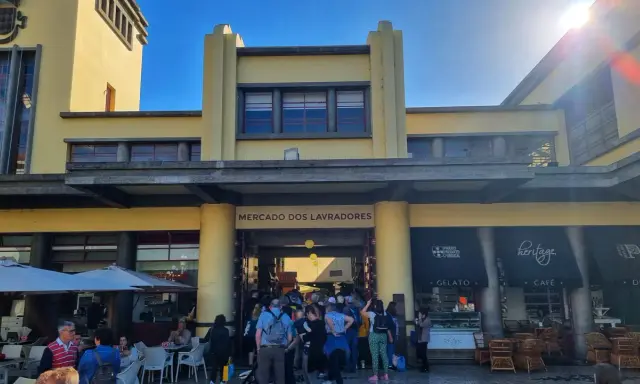 Menschen drängen sich vor dem Mercado dos Lavradores, einem gelben Gebäude mit Cafés und Geschäften.