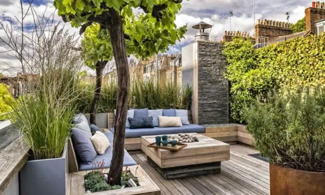 Un coin salon confortable pour aménager une terrasse avec des coussins bleus, une table basse en bois et une végétation luxuriante.