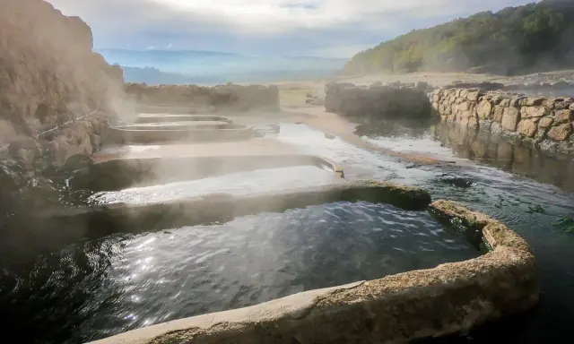 Tierras de vapor y agua en las termas naturales Galicia. Un paisaje sereno con piscinas escalonadas y muros de piedra.